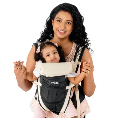 Smiling mother carrying a baby in a black Luvlap Elegant Baby Carrier with beige padding and straps, designed for comfortable and secure babywearing. Shows the baby facing towards the parent. From uSmile.toys." www.usmile.toys