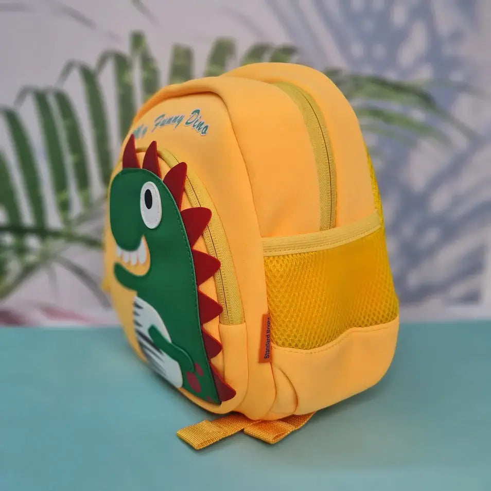 Small, yellow backpack for children featuring a large green dinosaur applique with red spikes and white teeth on the front pocket. Above the dinosaur is embroidered yellow cursive text that reads "My Funny Dino". The backpack has yellow straps and yellow mesh side pockets