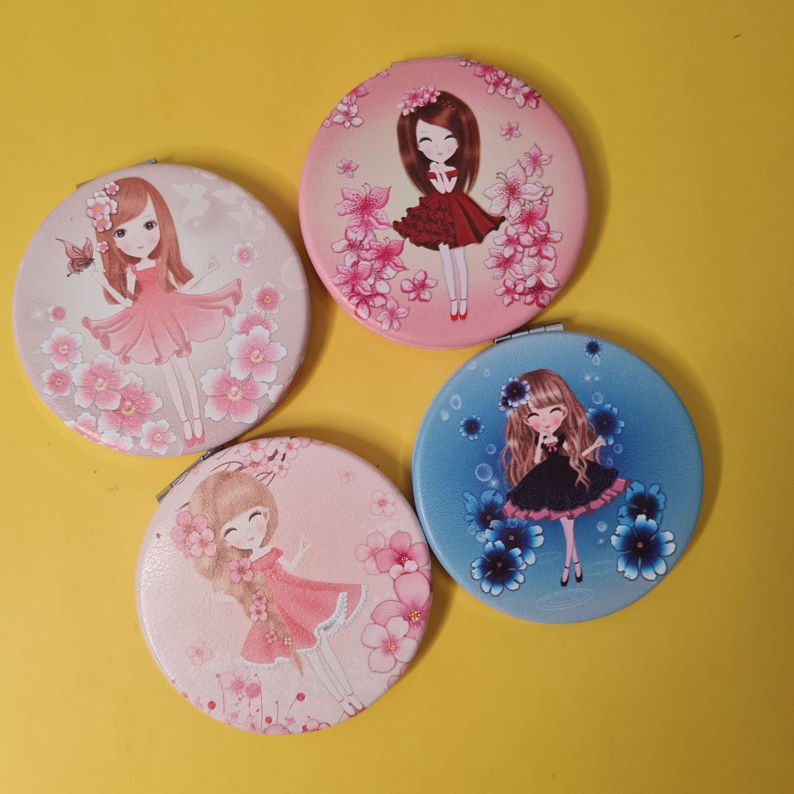 Four round compact mirrors with cartoon character designs on a yellow background