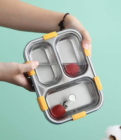 Premium quality stainless steel lunch boxes with colorful airtight lids featuring white, black, and yellow clasps, perfect for kids and adults, displayed neatly alongside healthy meals including rice, fried snacks, fresh fruits, and soup. These stylish and durable lunch containers are ideal for school, office, and travel use. Available at www.usmile.toys, your trusted online store for toys, kids stationery, return gifts, baby products, and essentials. Enhance your lunchtime experience with our leakproof, mu