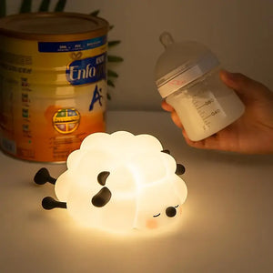Adorable glowing white silicone night lamp for kids, shaped like a little sleeping sheep with closed eyes and a peaceful expression, resting on a white surface. Ideal for a calming bedtime ambiance from uSmile.toys." www.usmile.toys