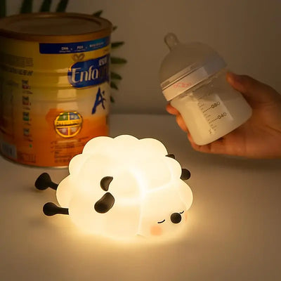 Adorable glowing white silicone night lamp for kids, shaped like a little sleeping sheep with closed eyes and a peaceful expression, resting on a white surface. Ideal for a calming bedtime ambiance from uSmile.toys." www.usmile.toys