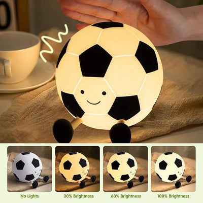 Adorable glowing white and black silicone night lamp for kids, shaped like a soccer ball (football) with a friendly smiley face and small legs, resting on a surface. Ideal for a sports-themed bedroom from uSmile.toys." www.usmile.toys