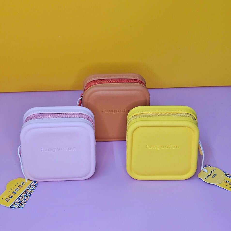 Three small rectangular bags in purple, brown, and yellow on a purple surface with a yellow background.