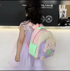 Usmile Toys pre-school backpack for kids, featuring an adorable light blue and green dinosaur with yellow spikes on a beige bag."www.usmile.toys