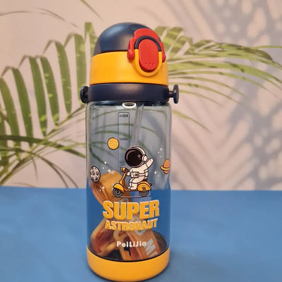 600ml astronaut-themed water bottle for kids featuring a leak-proof design and one-touch flip-open lid. The bottle has a transparent body with space and cartoon graphics, including the word 'SUPER' and an astronaut illustration. The cap is shown in a close-up inset, highlighting the one-key button for opening. The bottle is partially submerged in splashing water, emphasizing its leakproof and durable quality. Available in random colors, ideal for school or travel use