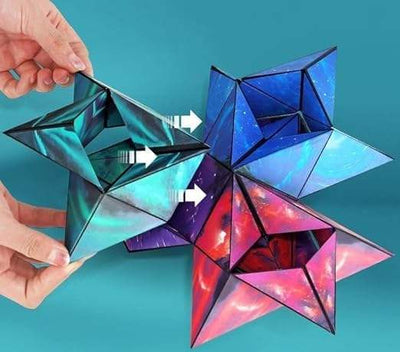 A photo of a boxed product called the “Changeable Magnetic Magic Cube.” The cube is displayed inside a unique packaging that emphasizes its geometric, triangular folding structure. The visible part of the cube has a vibrant, abstract blue design resembling swirling ocean or sky patterns. The box features various marketing phrases. The front side displays the name in bold white font: “Magic Cube,” with "Changeable" in red and "magnetic" in blue, highlighting its changeable and magnetic nature. The right side