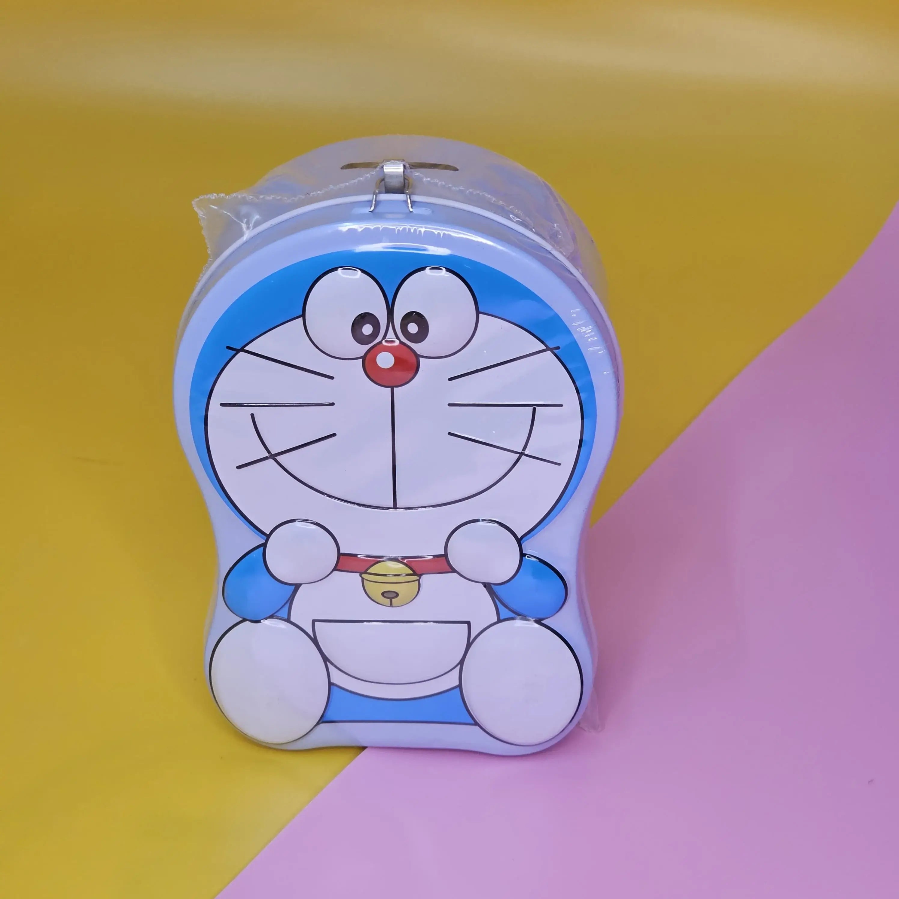 "Blue and white Doraemon-shaped metal money box (piggy bank) with a top slot for coins, featuring a lock and key for secure saving. Ideal gift for kids from uSmile.toys." www.usmile.toys