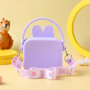 "Front view of a Usmile Toys girls' crossbody purse, made of purple silicone in a charming bunny shape, displayed among tropical leaves." www.usmile.toys