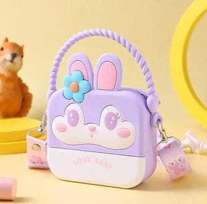 "Front view of a Usmile Toys girls' crossbody purse, made of purple silicone in a charming bunny shape, displayed among tropical leaves." www.usmile.toys